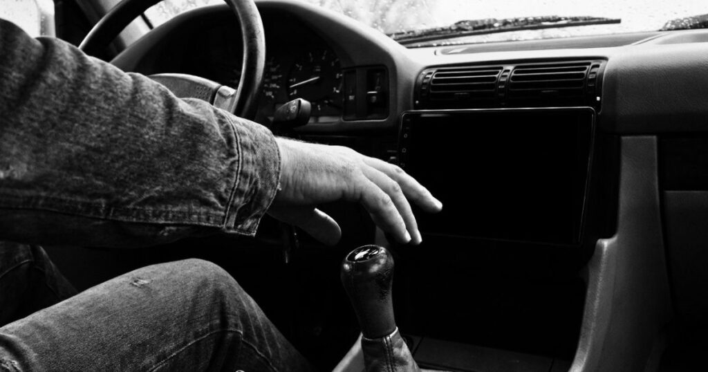 Hand hovering over a car gear shift with a blank navigation screen on the dashboard