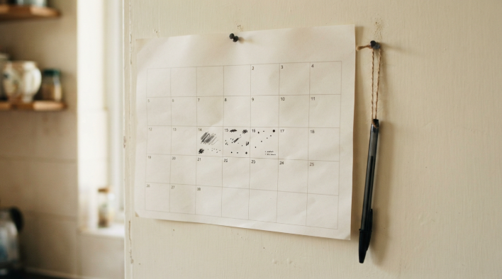Paper monthly calendar pinned on a kitchen wall with a pen on a string